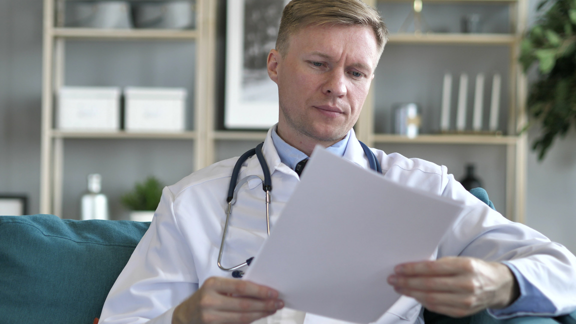Busy Doctor Reading Medical Report of Patient